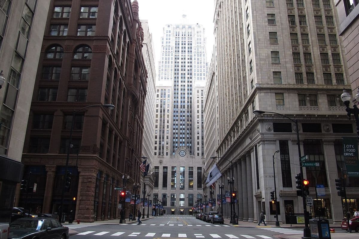 Edifício art déco da Chicago Board of Trade, com relógio na fachada, ao fim de uma rua estreita entre prédios altos no centro de Chicago