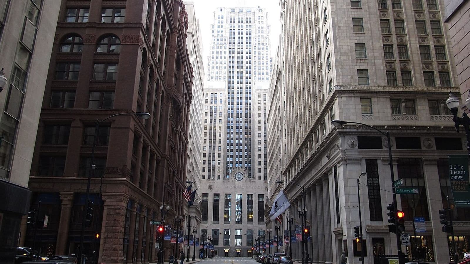 Edifício art déco da Chicago Board of Trade, com relógio na fachada, ao fim de uma rua estreita entre prédios altos no centro de Chicago