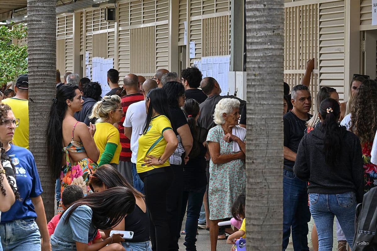 Eleitores, vários com camisas amarelas, em fila diante de salas de uma escola com listas de seções eleitorais coladas nas paredes