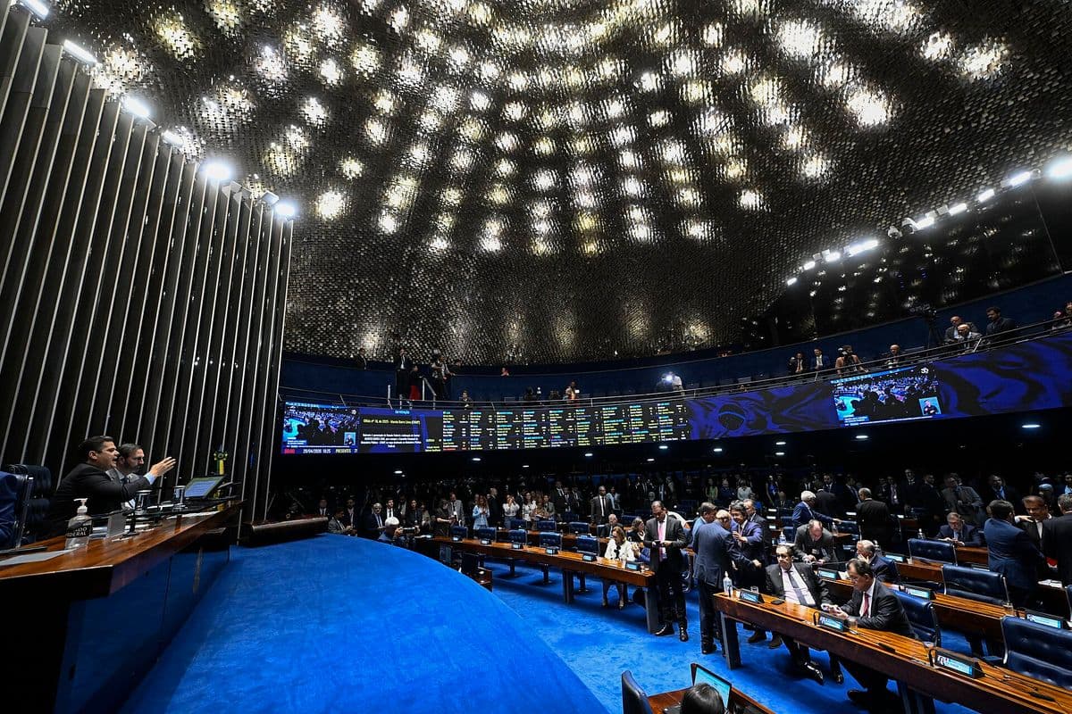 Plenário do Senado visto do alto, com senadores em pé entre as bancadas azuis e o painel eletrônico de votação ao fundo