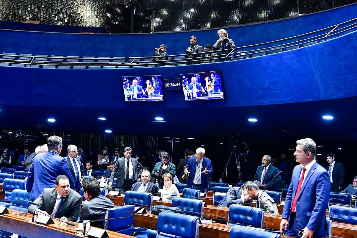 Plenário do Senado com senadores nas bancadas de cadeiras azuis, alguns de pé conversando, e fotógrafos na galeria