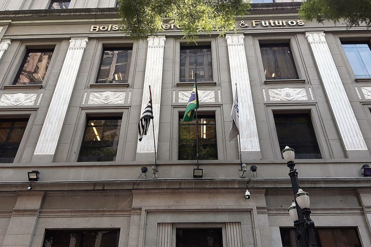 Fachada de pedra de prédio com colunas e o letreiro Bolsa de Mercadorias & Futuros, com bandeiras do Brasil e de São Paulo