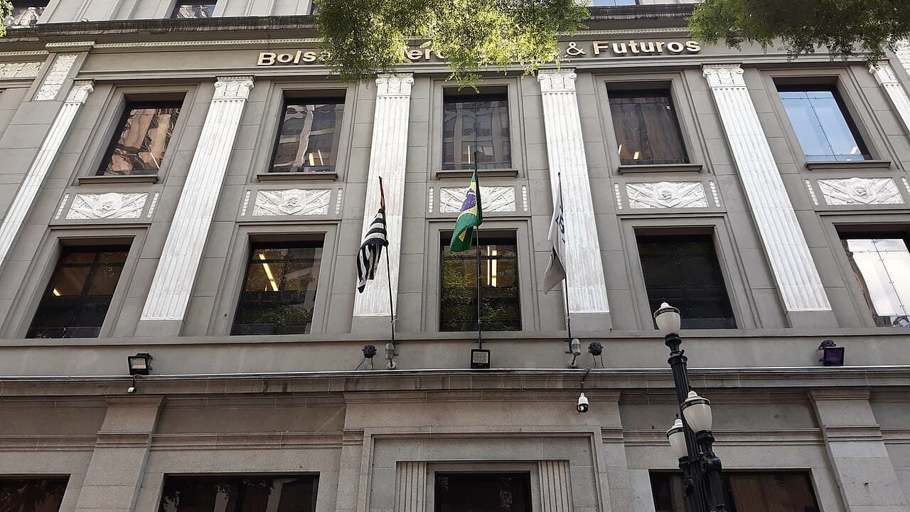 Fachada de pedra de prédio com colunas e o letreiro Bolsa de Mercadorias & Futuros, com bandeiras do Brasil e de São Paulo