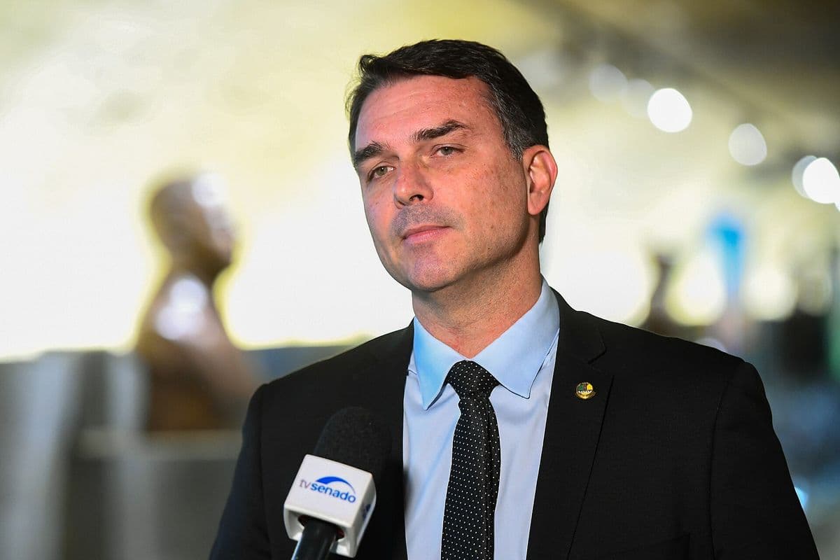Flávio Bolsonaro, de terno escuro e gravata, fala diante de um microfone da TV Senado