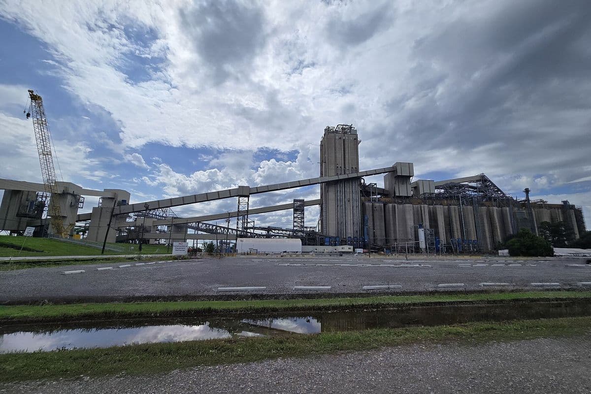 Complexo de silos de concreto e esteiras elevadas de um terminal de grãos, com guindaste à esquerda e céu nublado