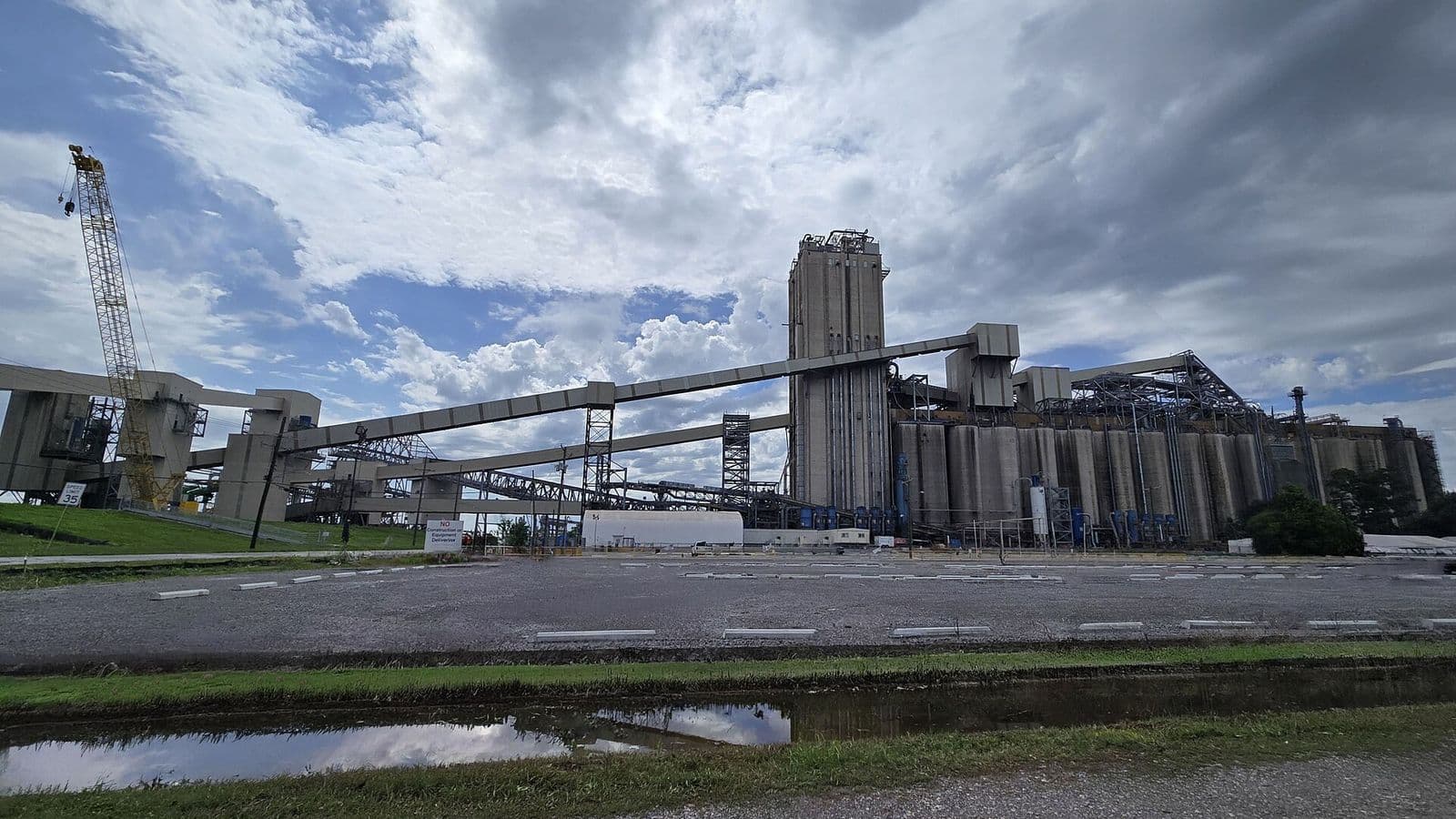 Complexo de silos de concreto e esteiras elevadas de um terminal de grãos, com guindaste à esquerda e céu nublado