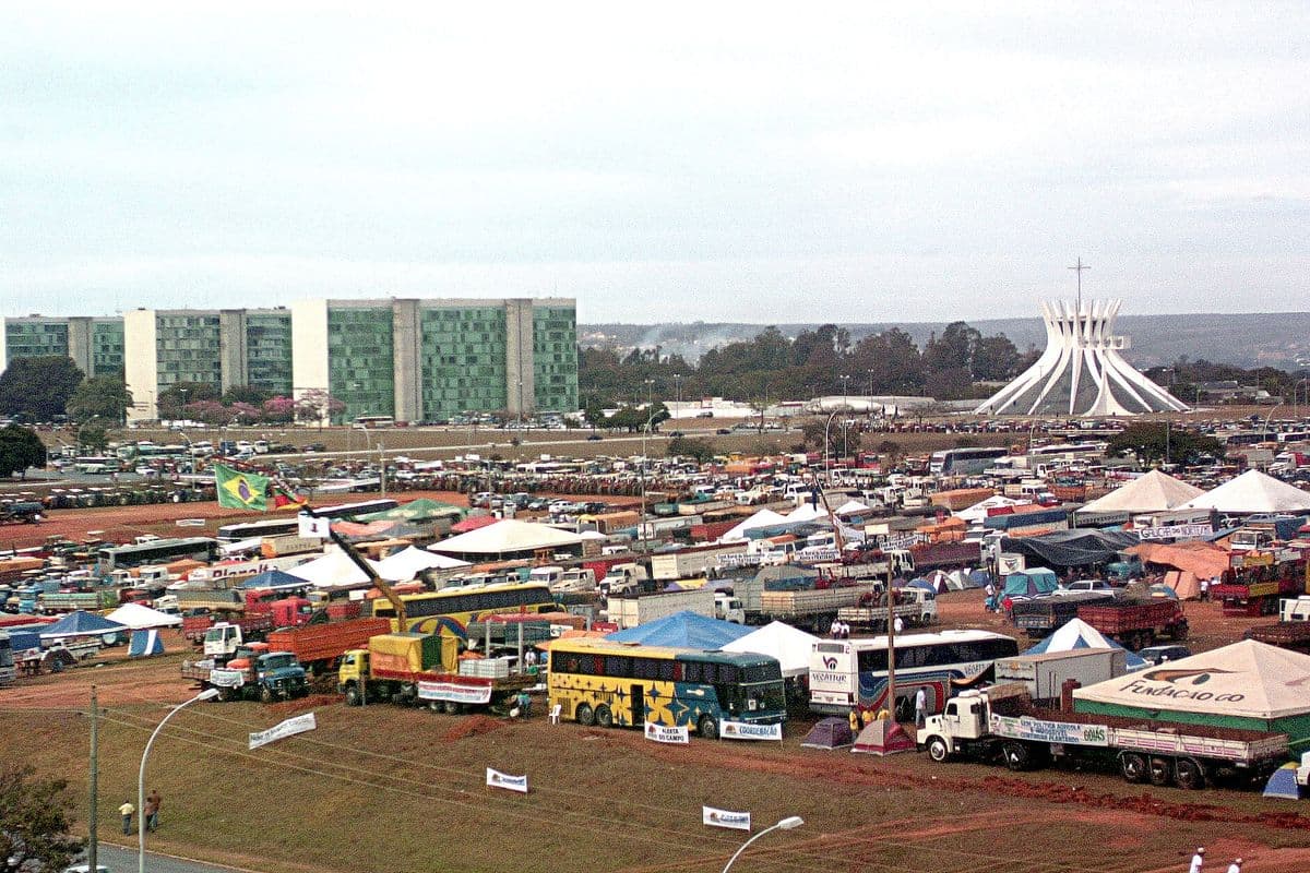 Centenas de tratores, caminhões, ônibus e tendas ocupam o gramado da Esplanada dos Ministérios, com os prédios dos ministérios à esquerda e a Catedral de Brasília à direita.