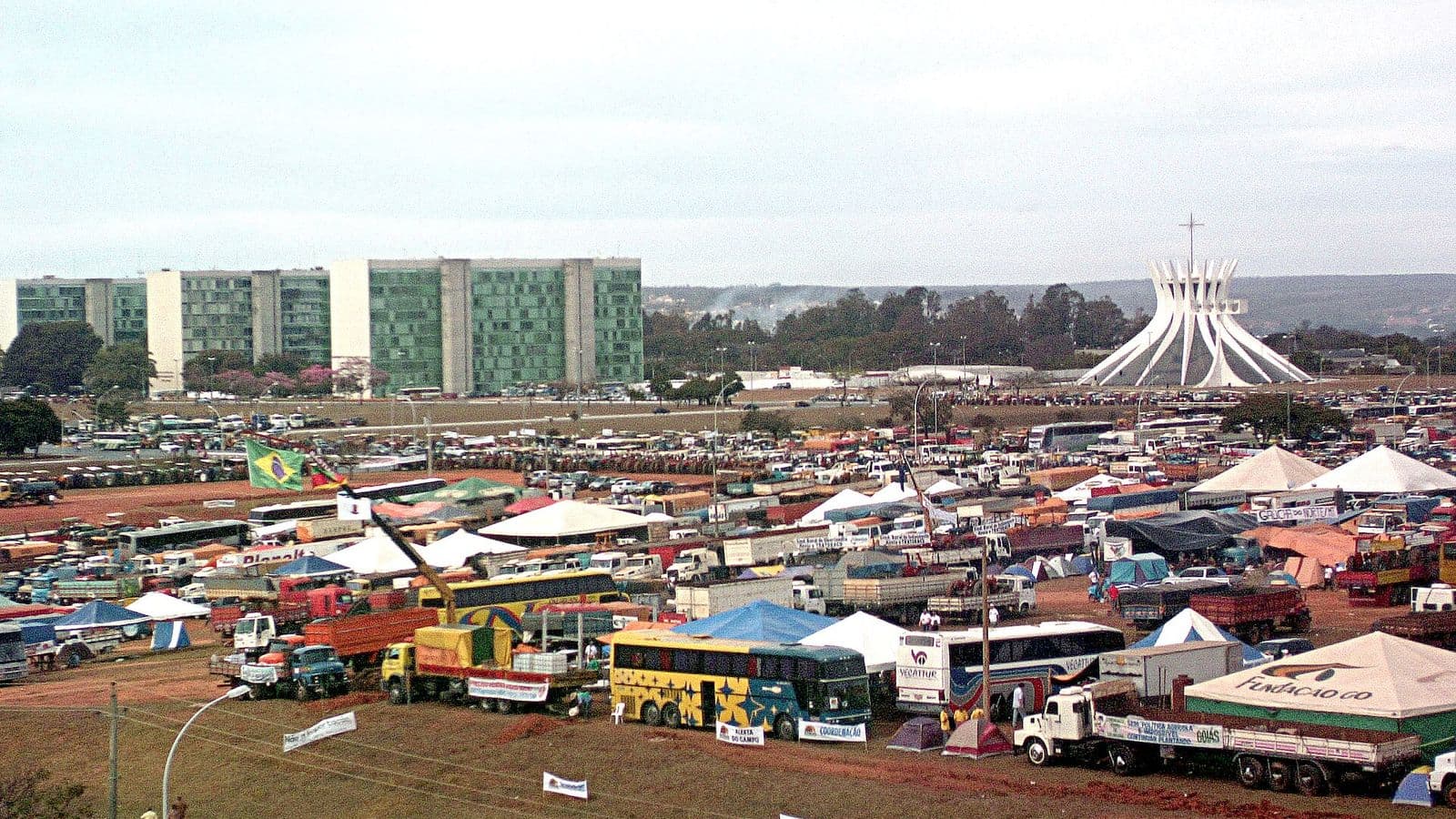 Centenas de tratores, caminhões, ônibus e tendas ocupam o gramado da Esplanada dos Ministérios, com os prédios dos ministérios à esquerda e a Catedral de Brasília à direita.