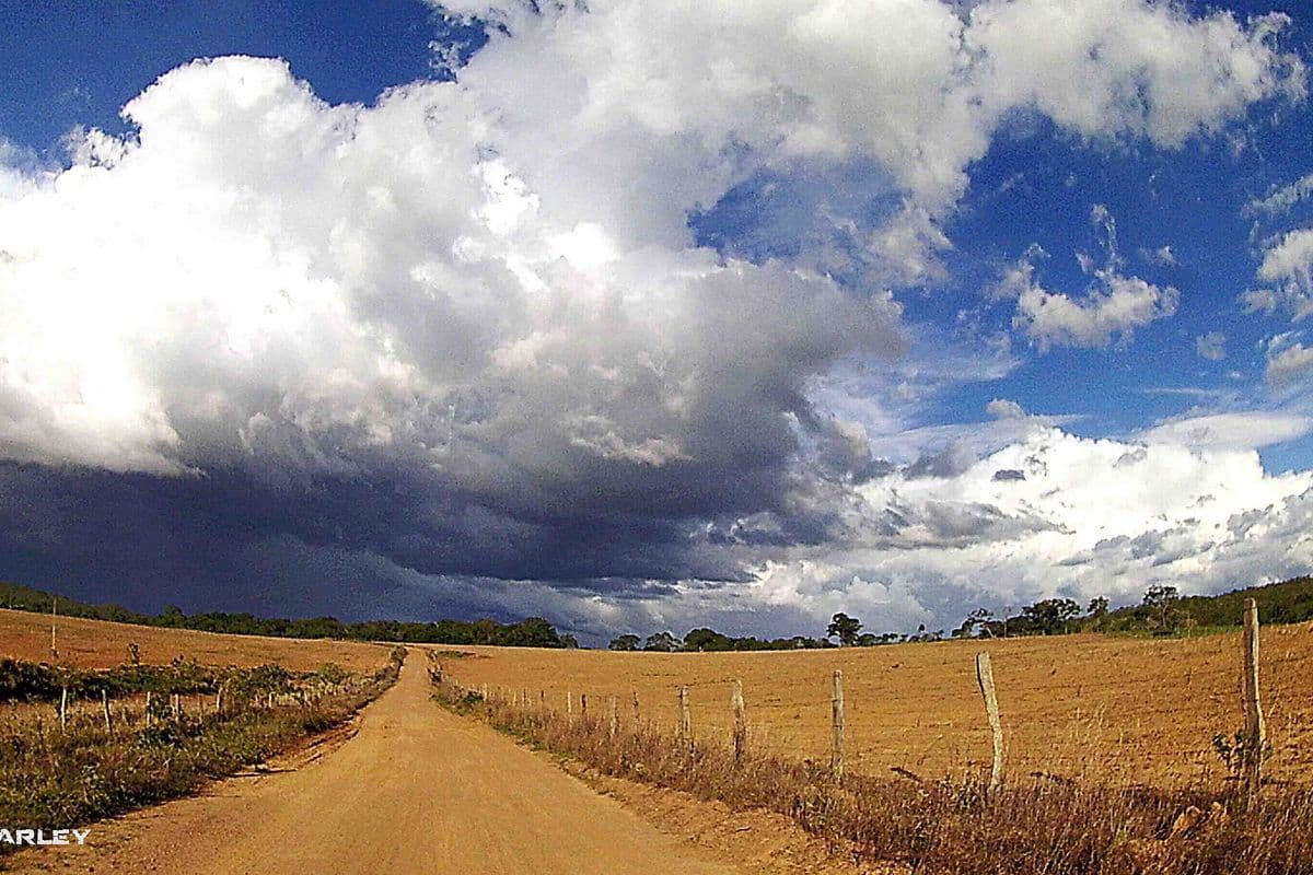 Estrada de terra entre pastos secos sob nuvens escuras de tempestade e céu azul em área rural de Goiás